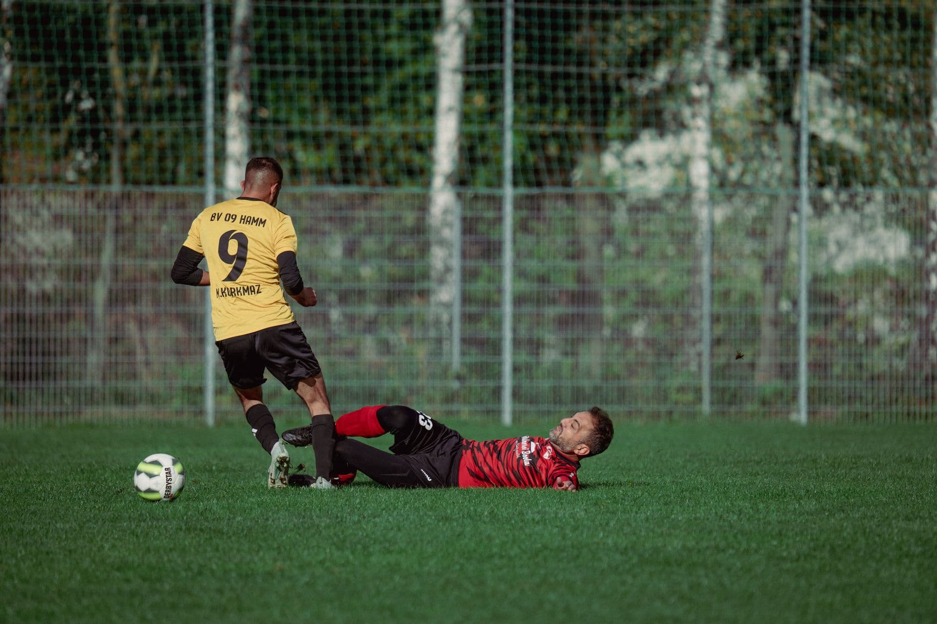 Two grassroots football players challenging for the ball mid-tackle on a grass pitch